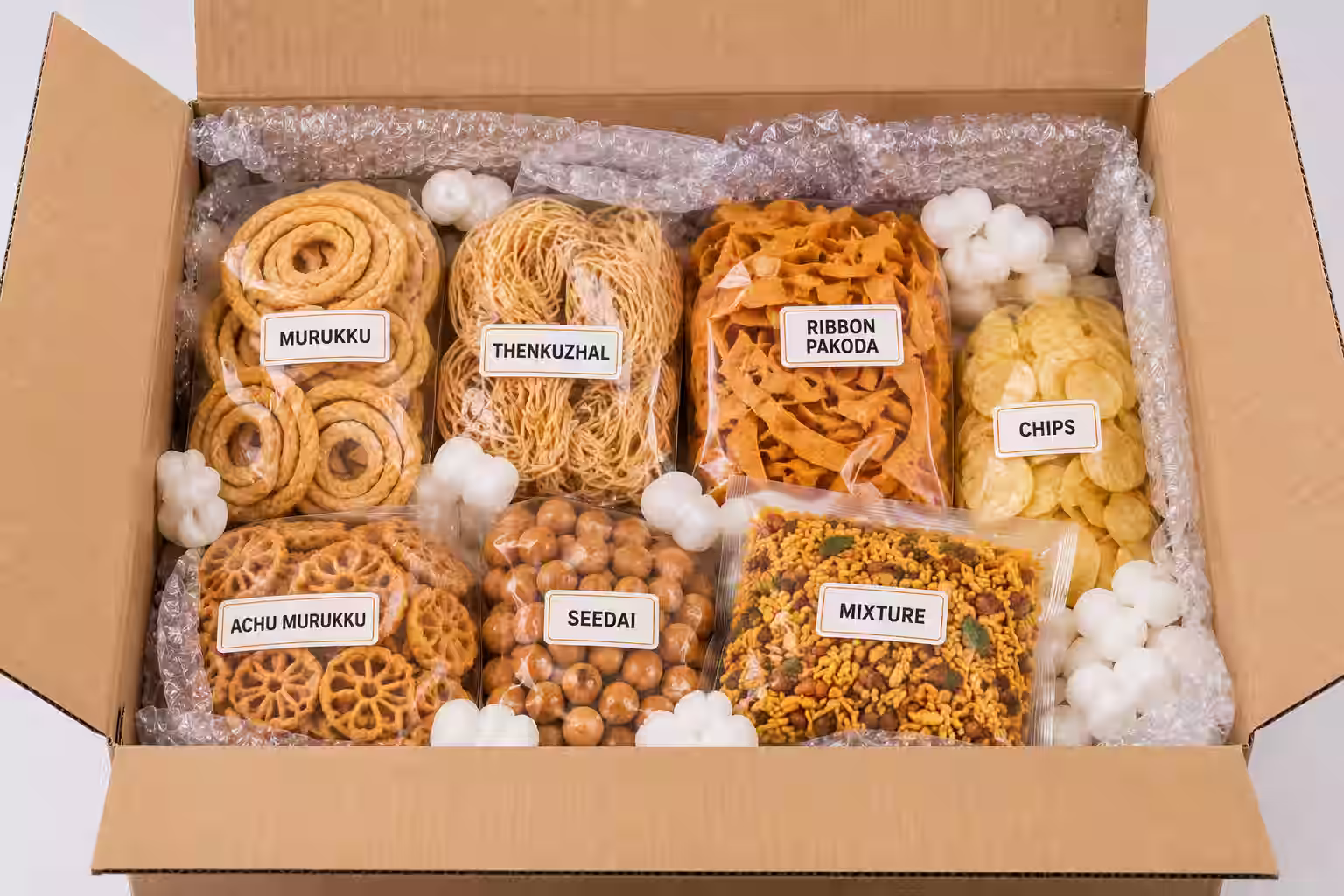 Homemade Indian snack varieties packed for international courier - labelled packs of murukku, thenkuzhal, ribbon pakoda, achu murukku, seedai, mixture and chips cushioned in an export carton